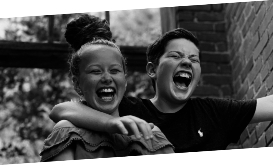 Schwarz-weiß-Bild zweier Kinder, der Junge hat den Arm um die Schulter des Mädchens gelegt und beide lachen herzlich